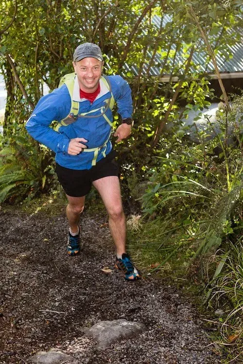 A man is running down a dirt path in the woods.