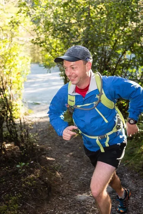 A man in a blue jacket and hat is running down a trail.