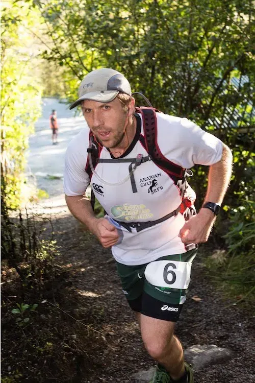 A man wearing a white shirt with the number 6 on it is running down a trail.