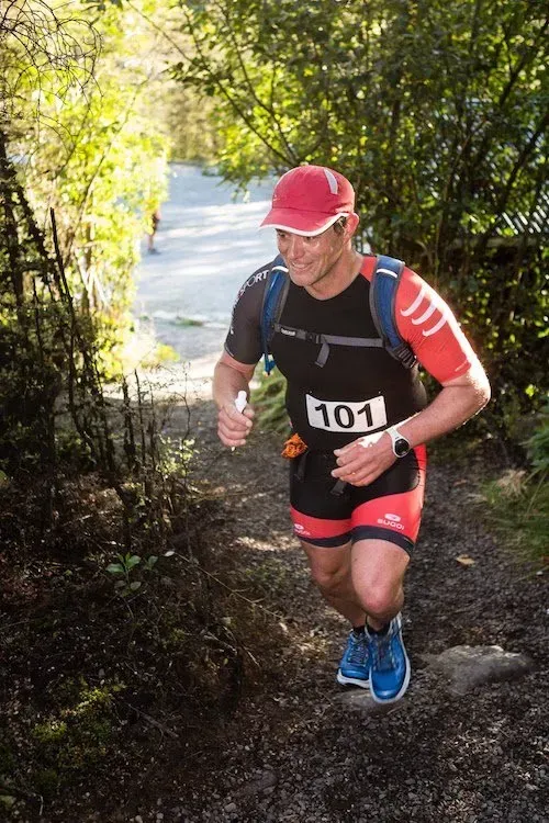 A man is running up a hill in the woods.