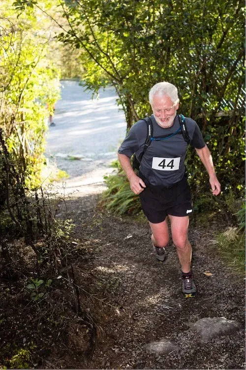 A man with a beard is running down a trail.