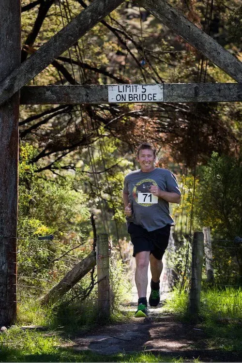 A man is running across a bridge in the woods.