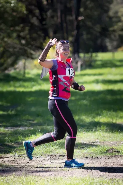 A woman in a pink shirt and black pants is running in a park.