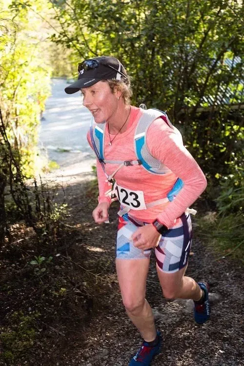 A woman is running down a trail in the woods.