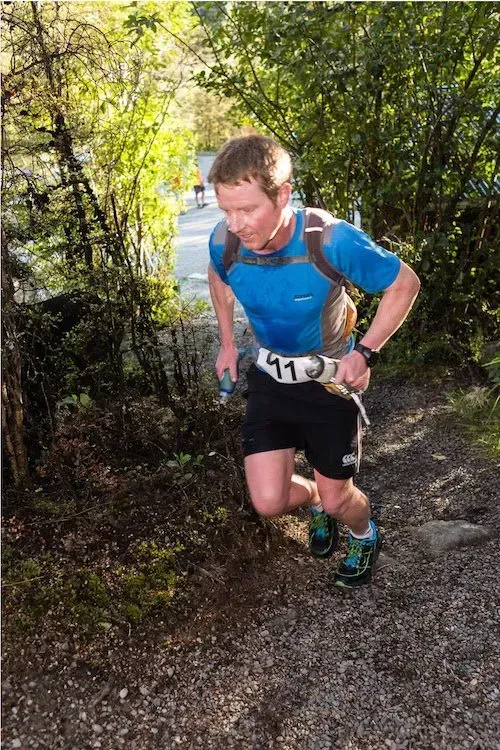 A man in a blue shirt and black shorts is running down a dirt path.
