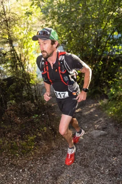 A man is running down a trail in the woods.