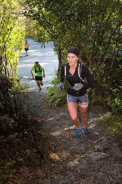 A woman is running up a hill in the woods.
