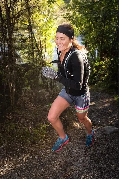 A woman is running on a trail in the woods.