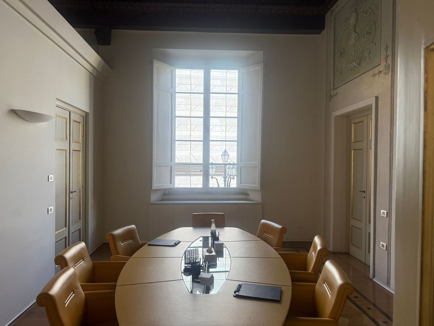 Sala conferenze con tavolo ovale, sedie in pelle, ampia finestra e pannello decorativo a parete.