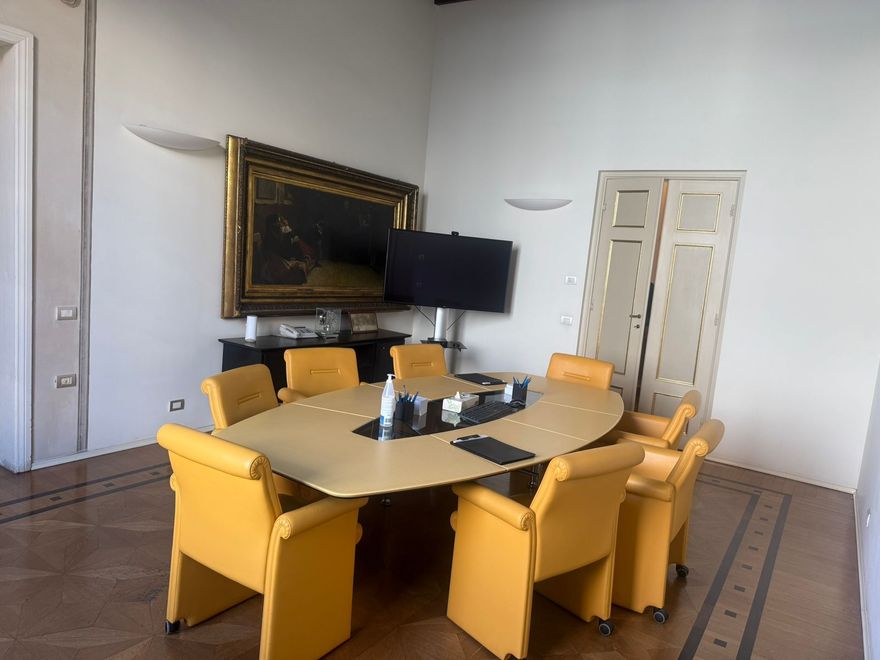 Sala conferenze con un grande tavolo ovale, sedie gialle e un dipinto incorniciato alla parete.
