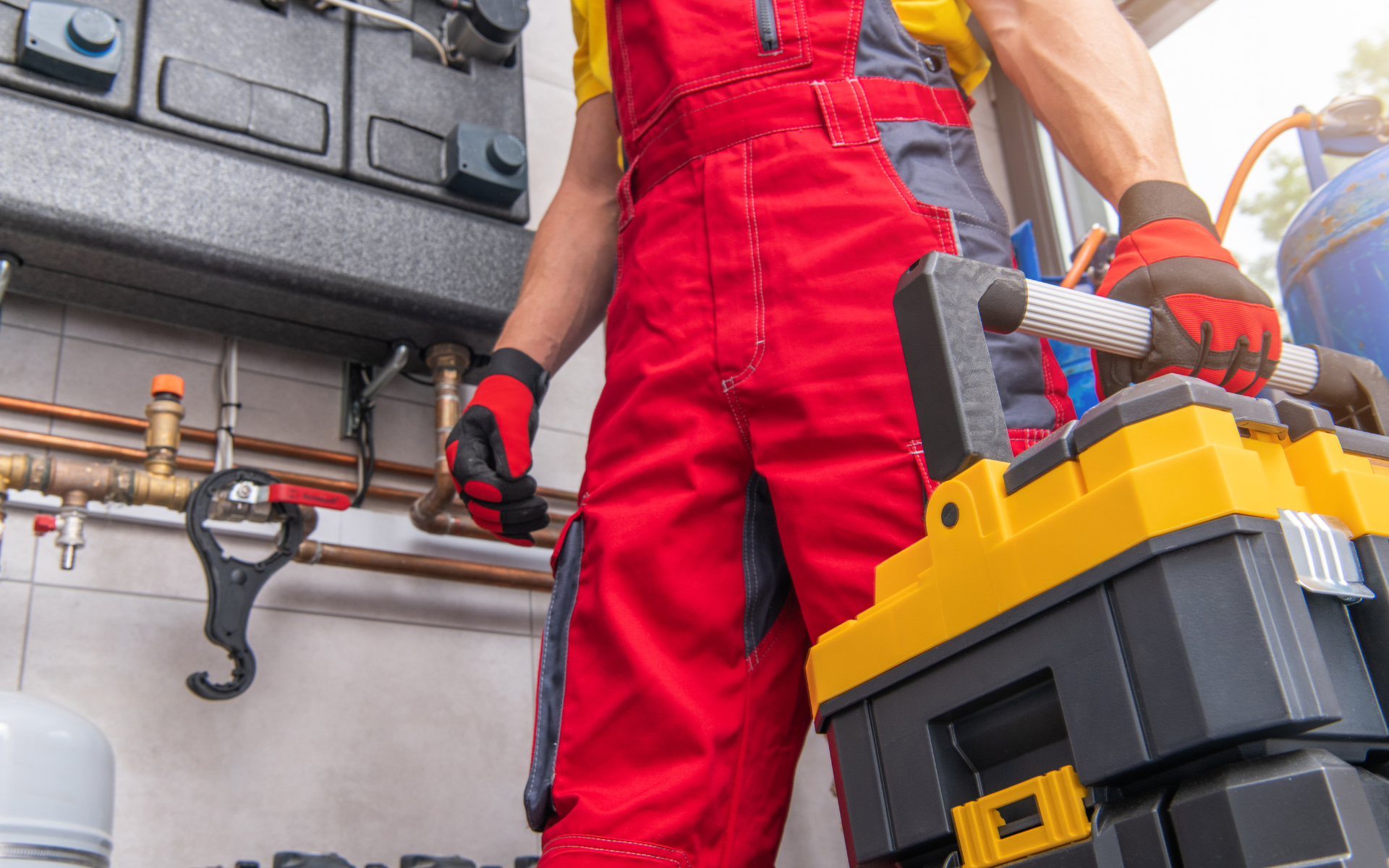 A man in red overalls is holding a toolbox in a room.