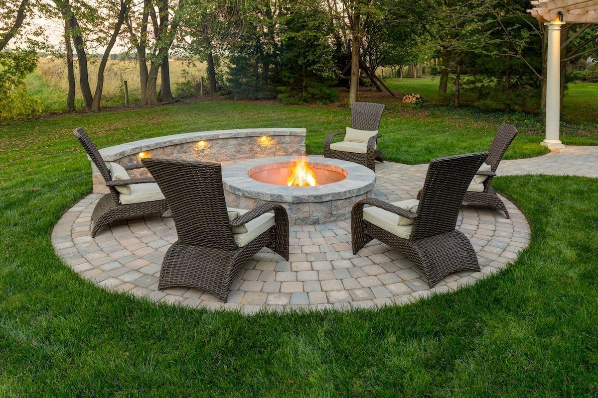 A fire pit in the middle of a patio with chairs around it.