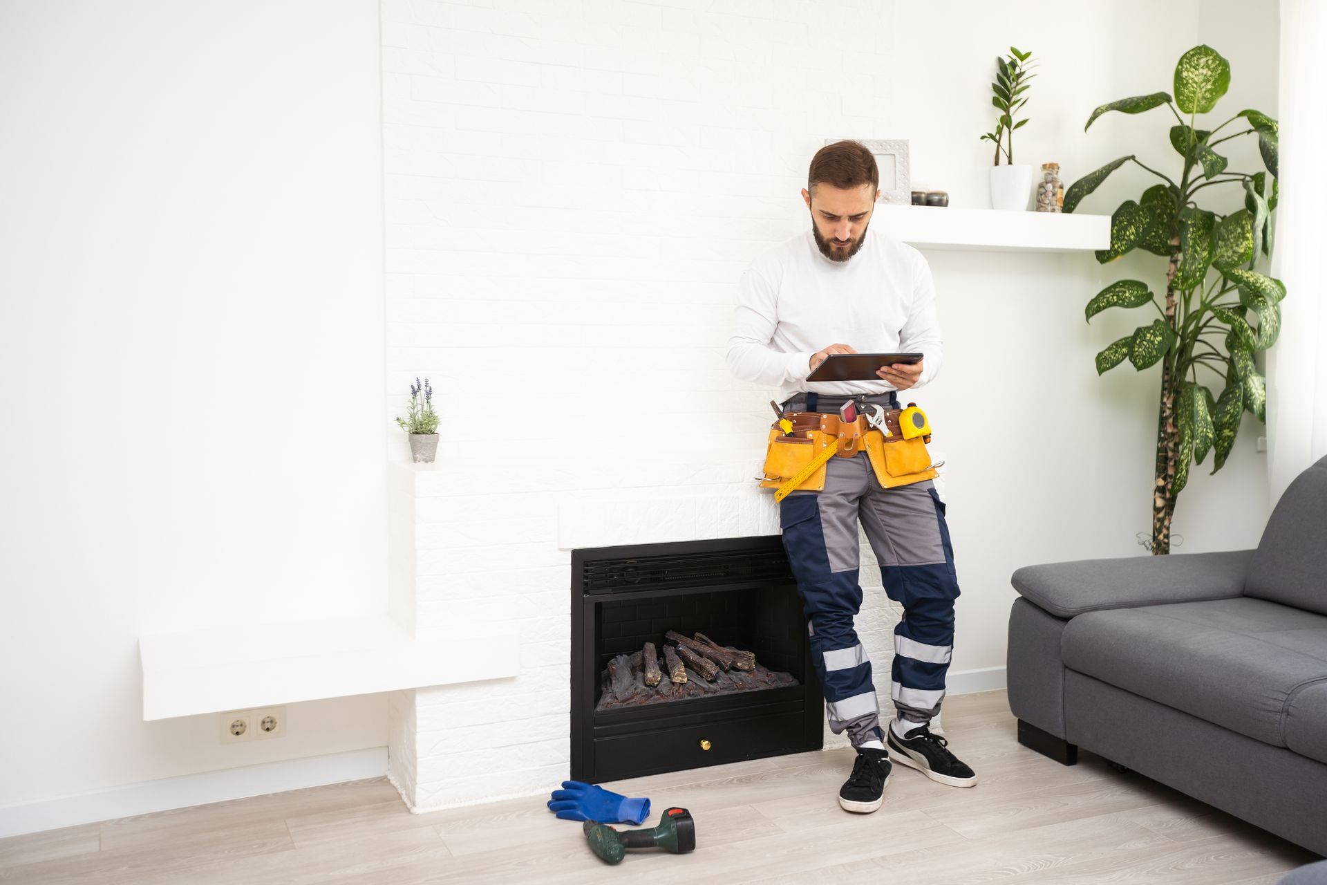 A man is standing next to a fireplace in a living room looking at a tablet.