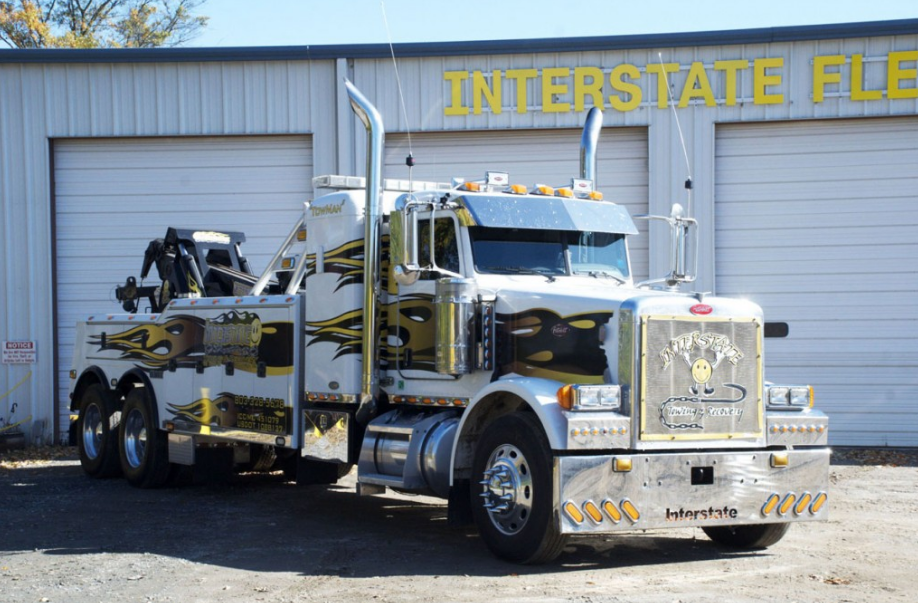 A tow truck is parked in front of a building that says interstate fleet