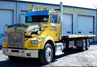 A yellow tow truck is parked in front of a building that says interstate leet services