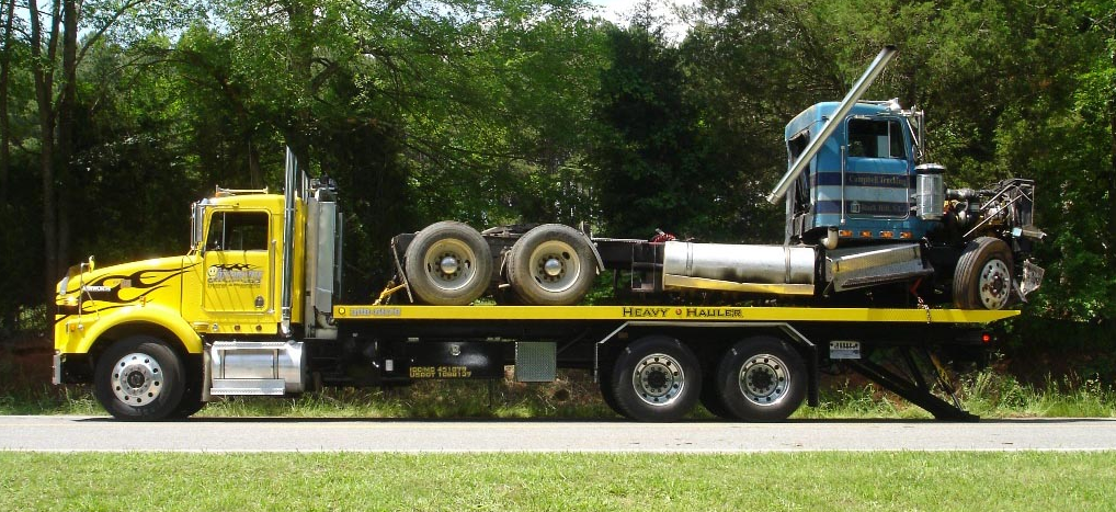 A yellow tow truck with a blue truck on the back