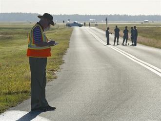 A man in a safety vest is standing on the side of a road