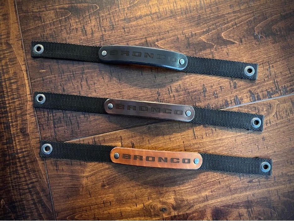 Three leather Bronco wristbands on a wood table, each with the word 