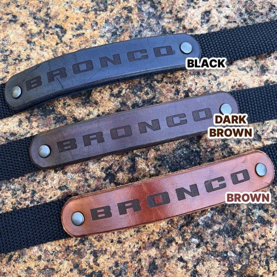 Three leather Bronco wristbands on a wood table, each with the word 