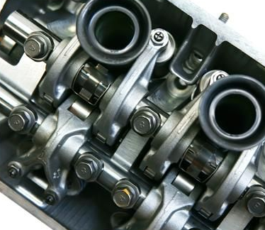 Vista ravvicinata dall'alto di componenti metallici di un motore a combustione interna, tra cui bilancieri e molle delle valvole.