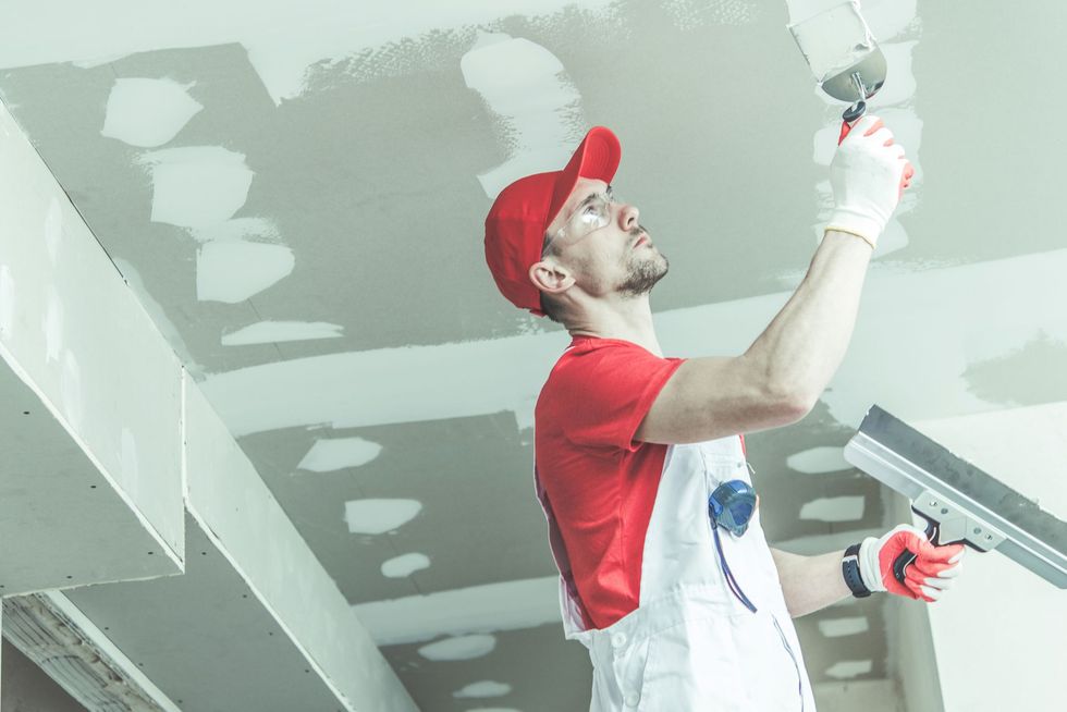 A man is plastering a ceiling with a spatula.