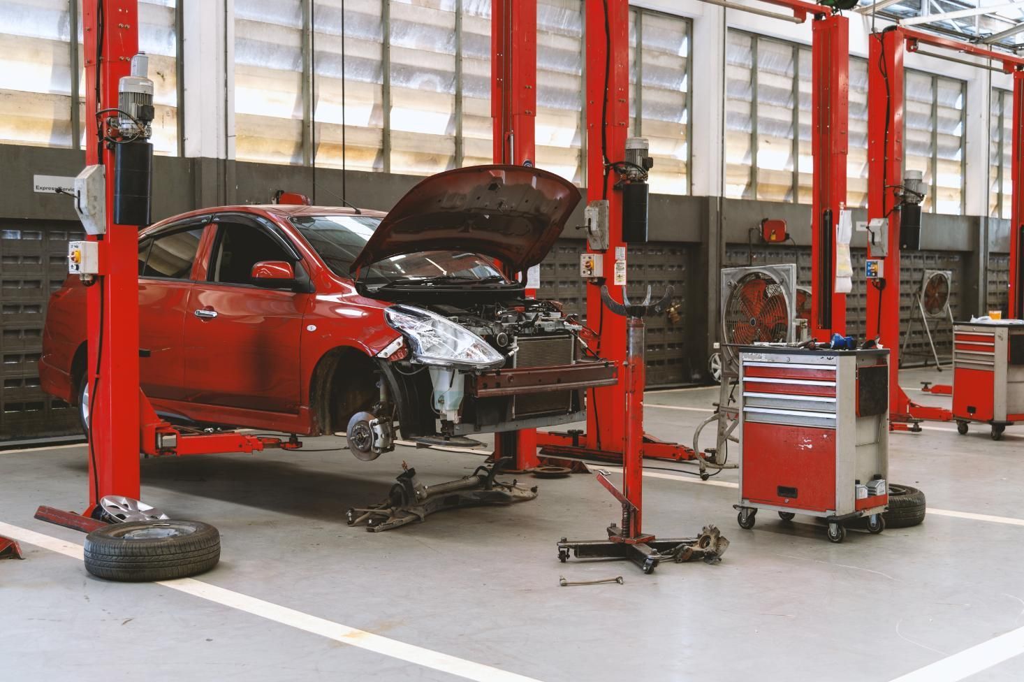 A red sedan with its hood open and wheels removed is raised on a hydraulic lift.