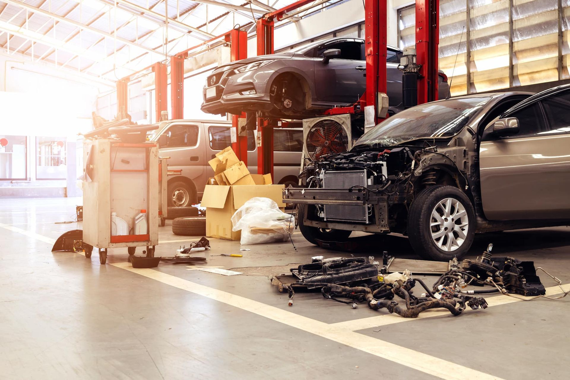 An auto repair shop with a car on a lift, a disassembled car in the foreground.