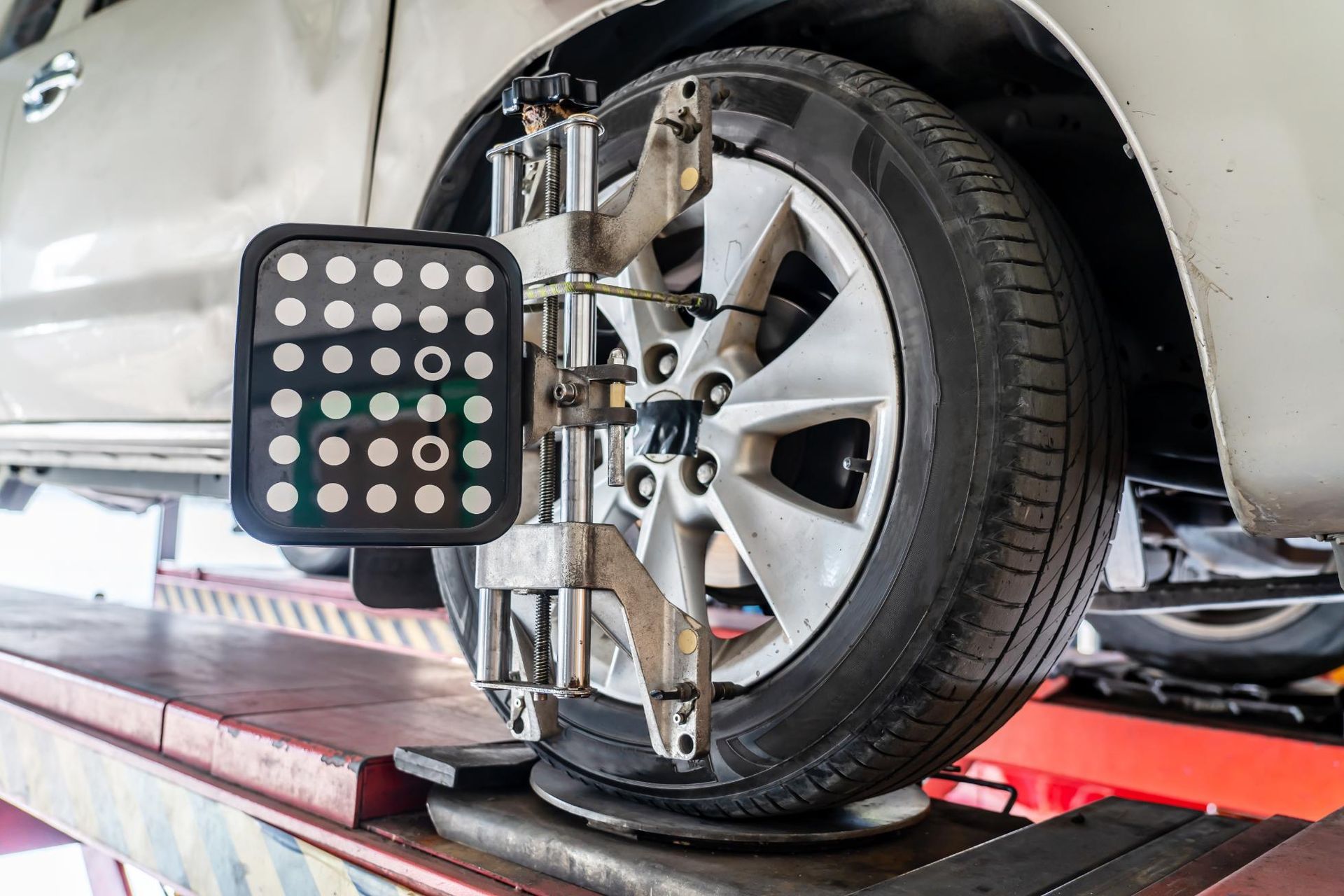 A wheel alignment target sensor mounted to the alloy rim of a car tire on an auto repair shop lift.