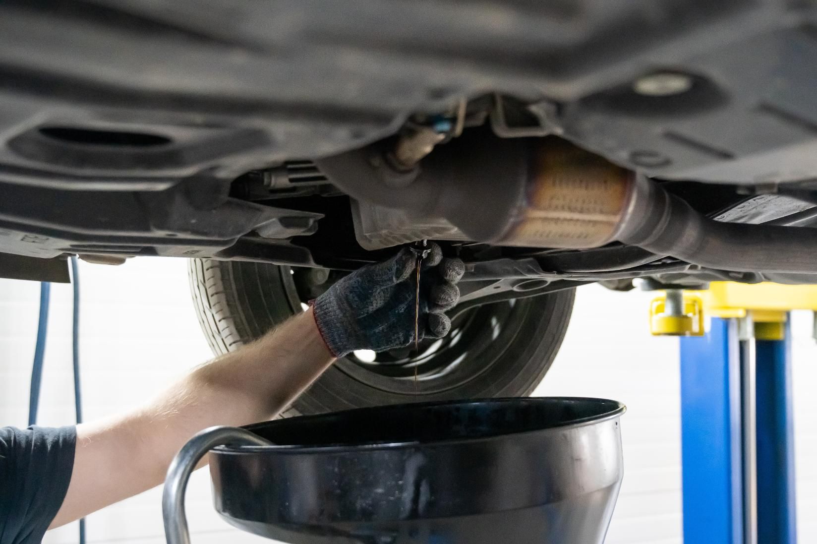 A gloved hand removes a plug from a vehicle's undercarriage to drain oil.