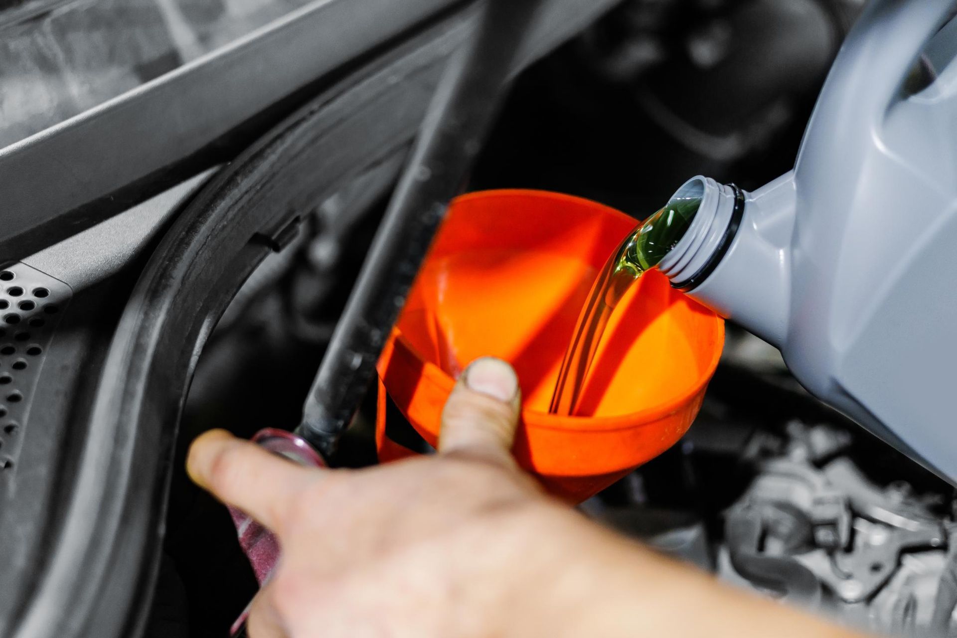 A hand holding an orange funnel while pouring green liquid into a car engine.