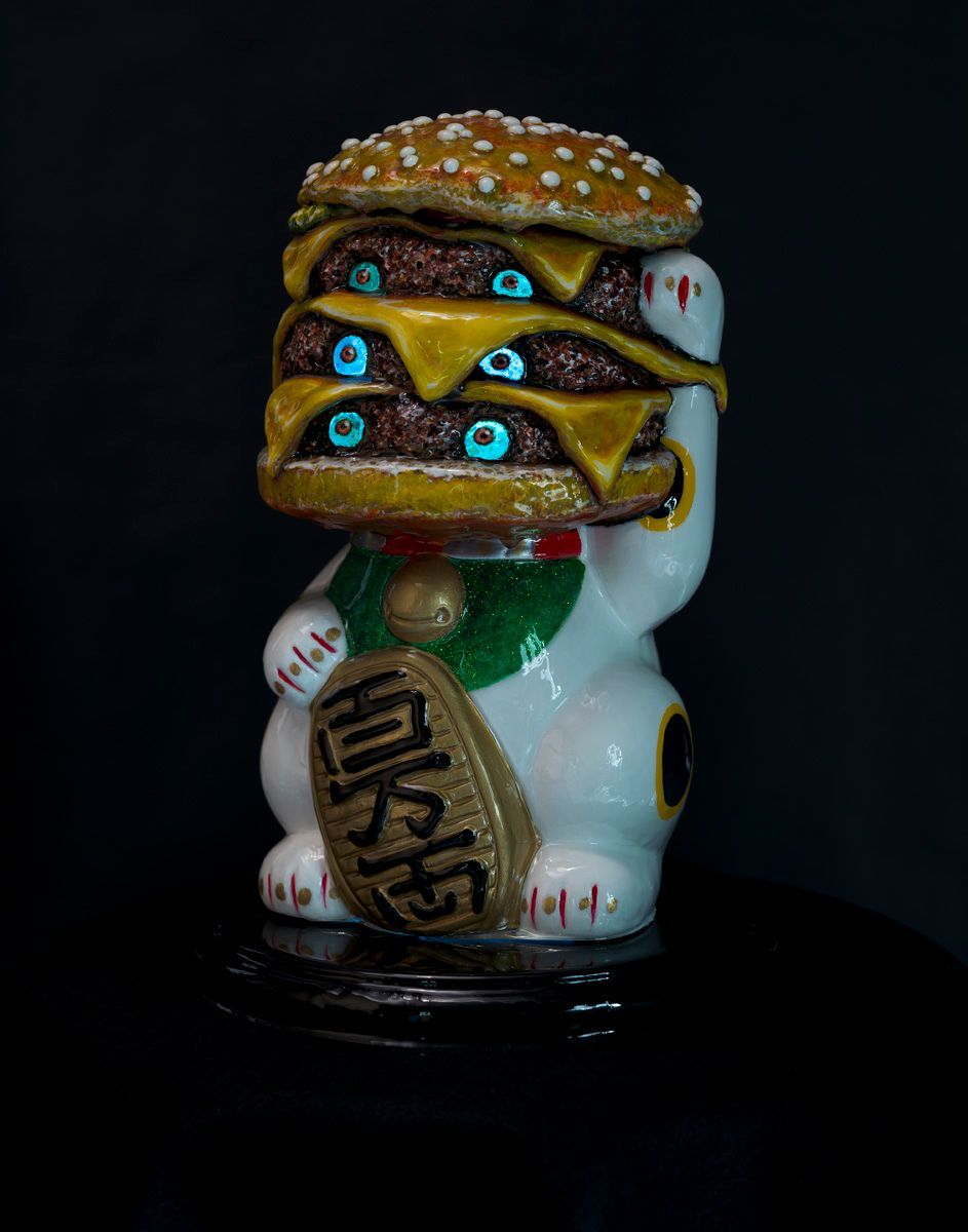 Art by Rich M Stevens. Stacked cheeseburger figurine on a white lucky cat statue against a black background