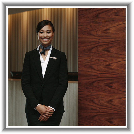 A woman in a suit is smiling in front of a wooden wall