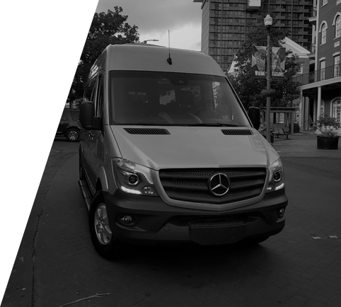 A mercedes van is parked on the side of the road in front of a building.