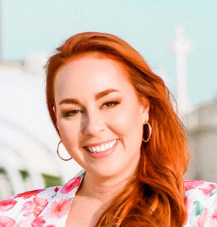 A woman with red hair is smiling and wearing hoop earrings