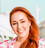 A woman with red hair is smiling and wearing hoop earrings