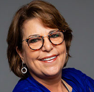 A woman wearing glasses and a blue shirt is smiling for the camera.