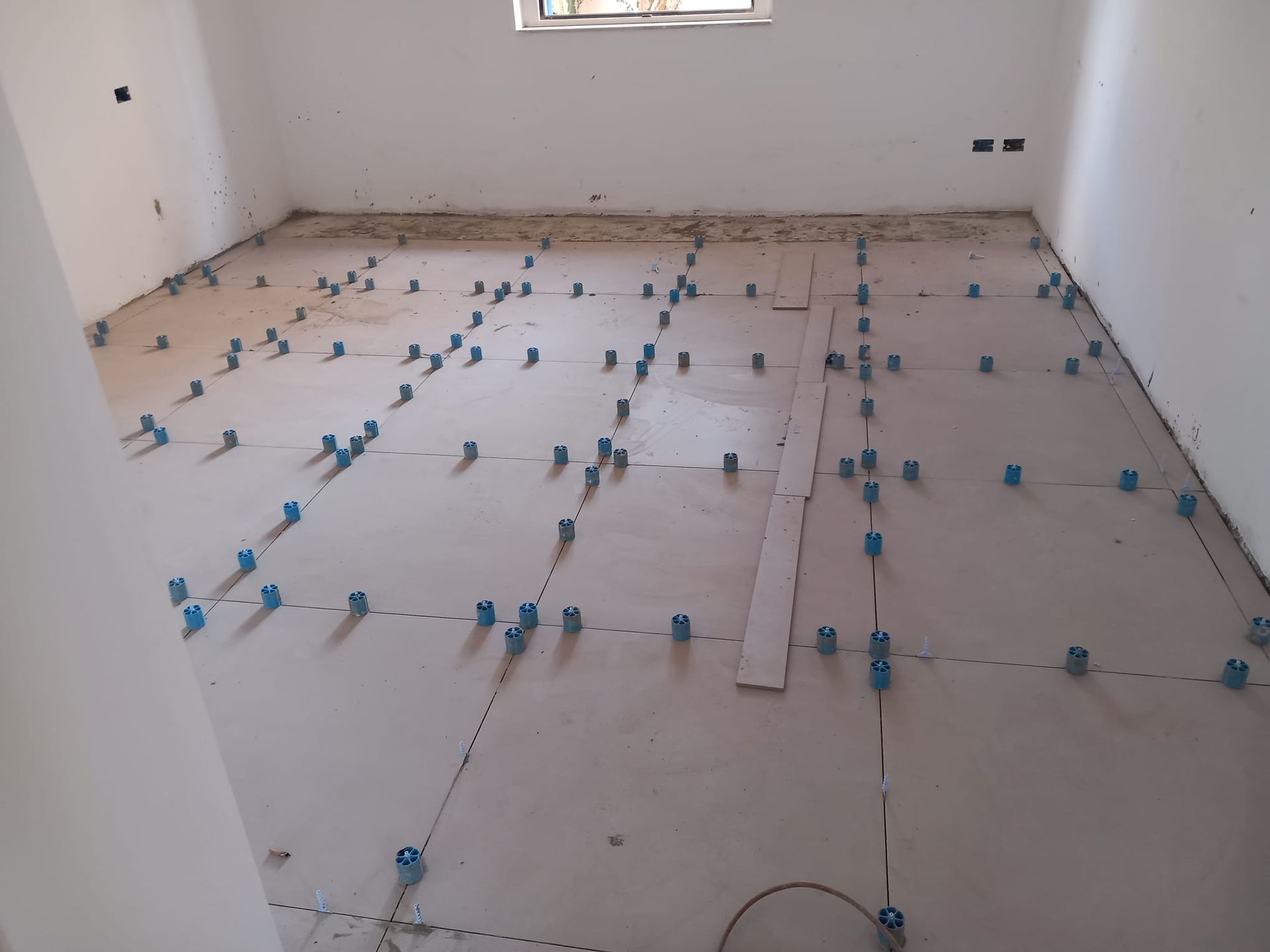 Uomo inginocchiato che installa piastrelle per pavimenti con sistema di livellamento in un ambiente interno.