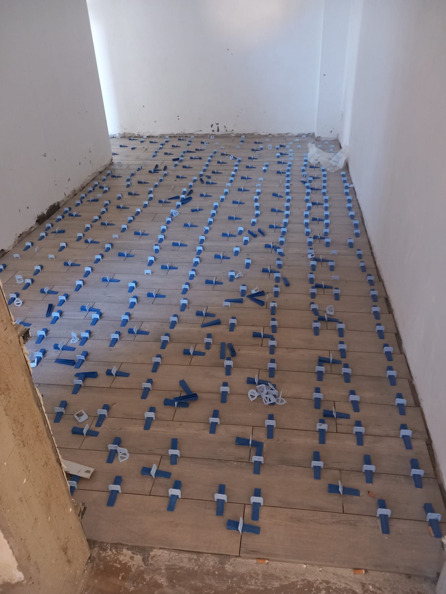 Uomo inginocchiato che installa piastrelle per pavimenti con sistema di livellamento in un ambiente interno.