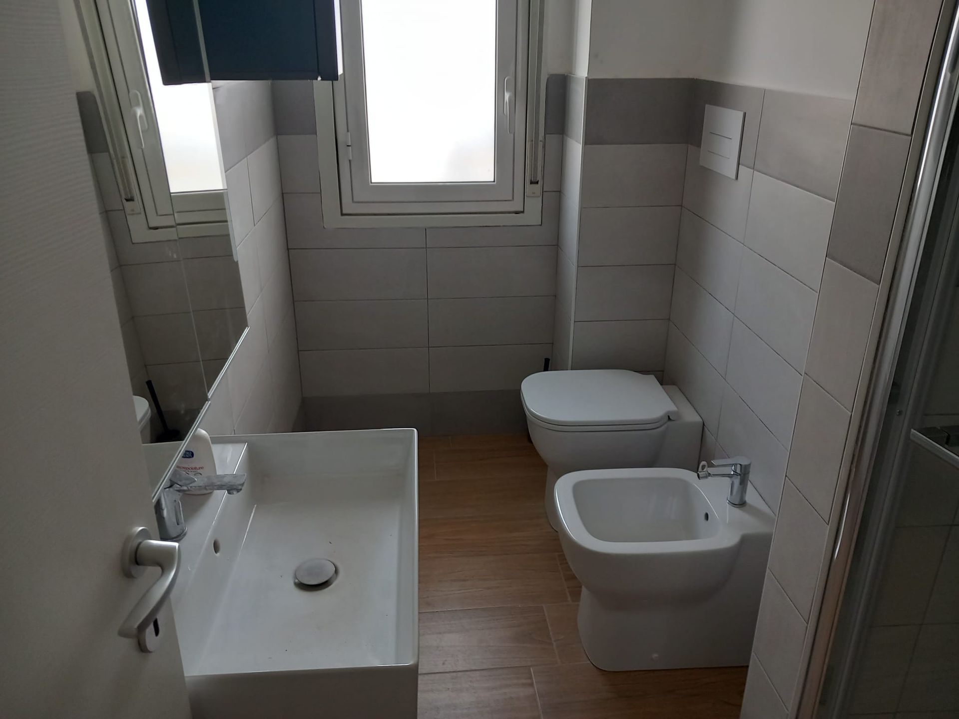 Bagno moderno con mobile lavabo in legno, piastrelle grigie, doccia in vetro e vasca.