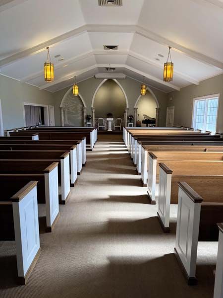 Interior of a church with wooden pews, white trim, and arched alcove. Two hanging lights.