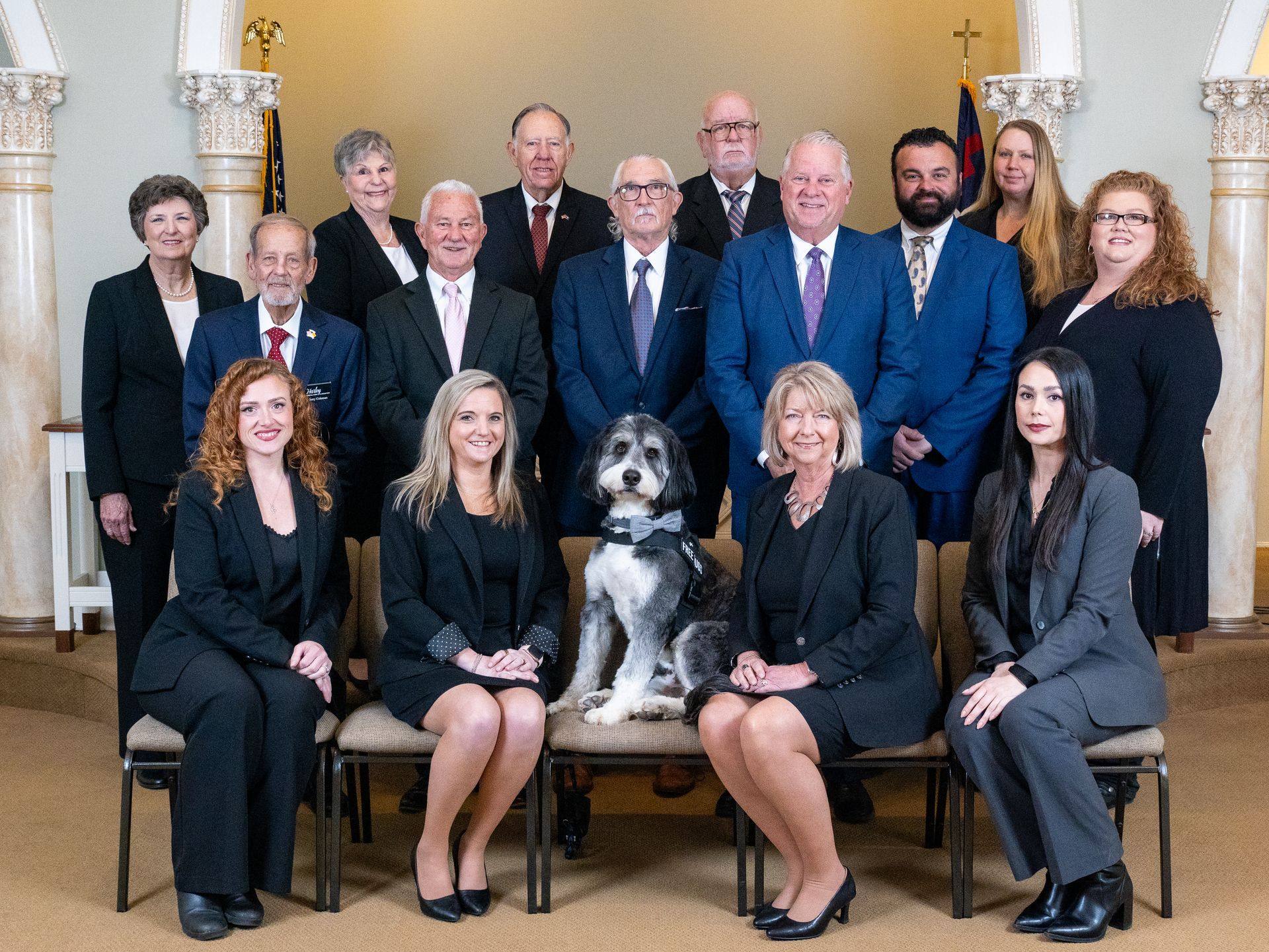 A group of people in suits posing in front of a brick building with columns and windows.
