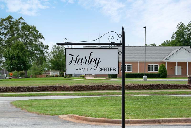 Sign for Harley Family Center. White sign with black text, ornate black pole in front of a building and green lawn.