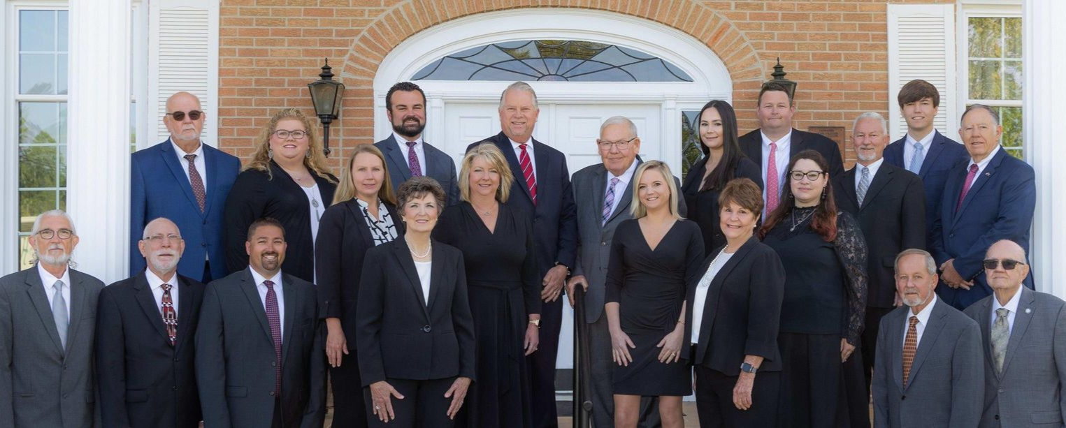 A group of people in suits posing in front of a brick building with columns and windows.