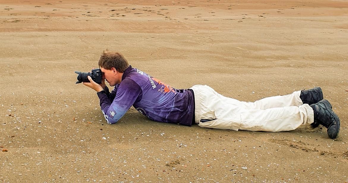 Photographer Lying on Beach, Aiming Camera — Up Here Photography in Rosebery, NT