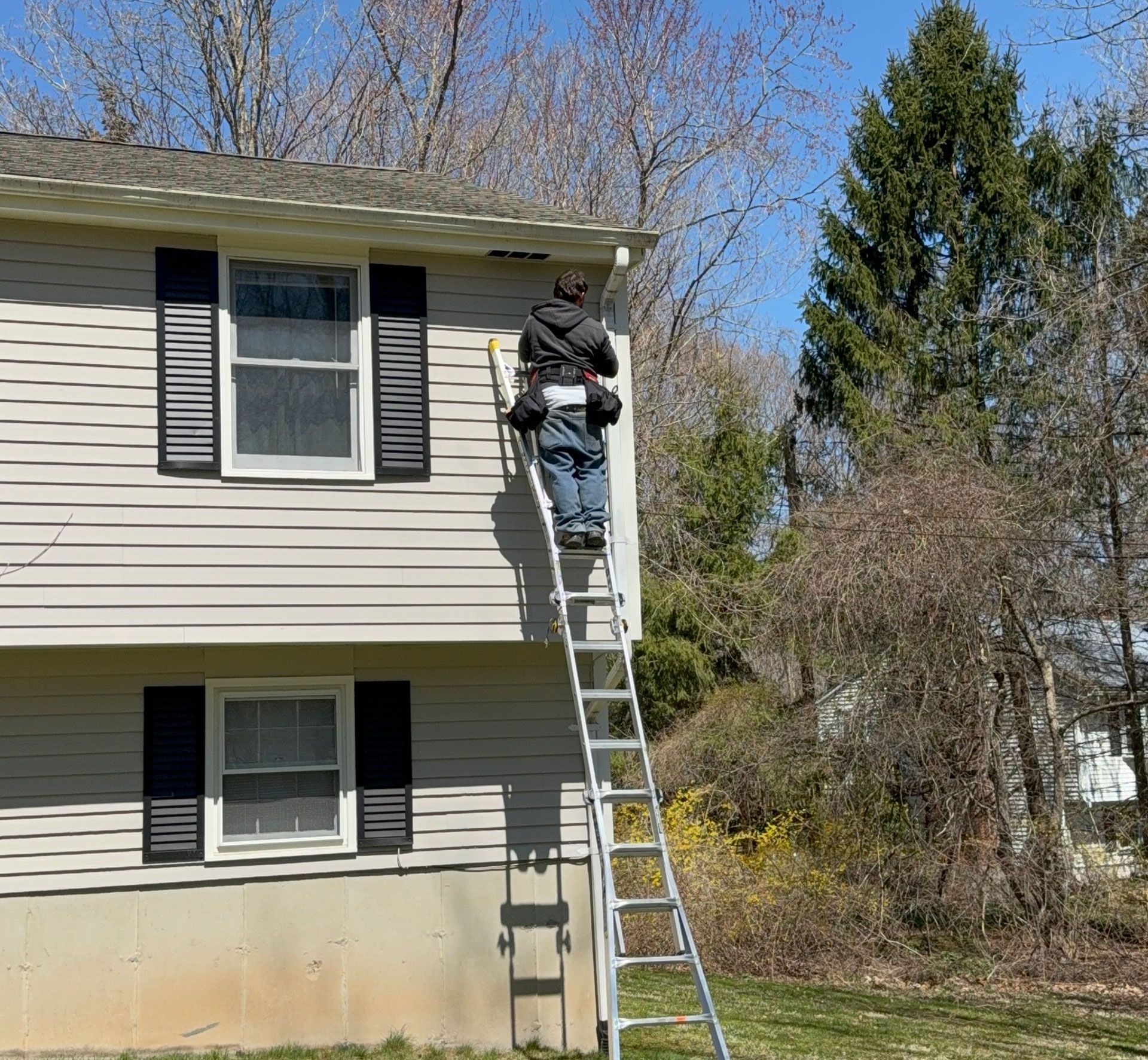 Brick house with white siding beside leafless trees under a blue sky