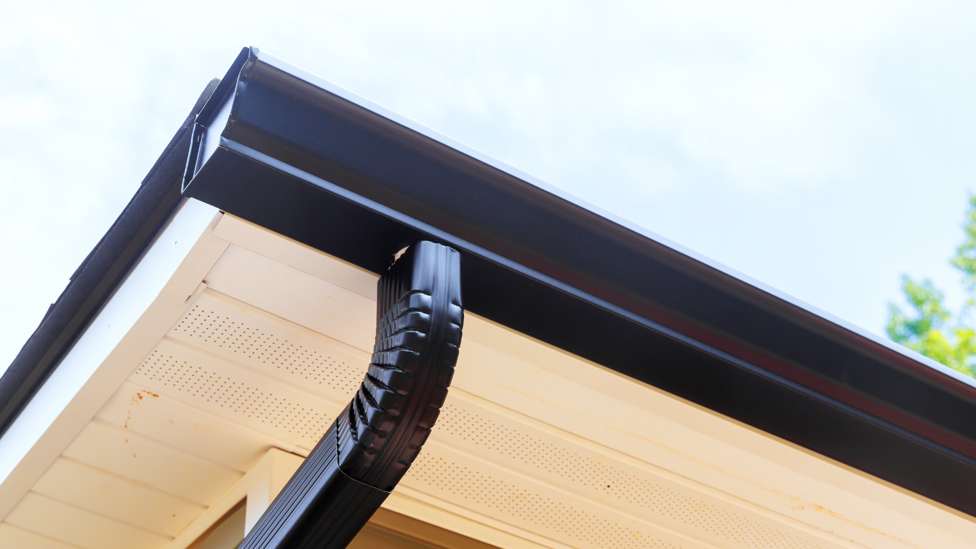 Person in a red jacket on a ladder cleaning a roof gutter against a blue sky