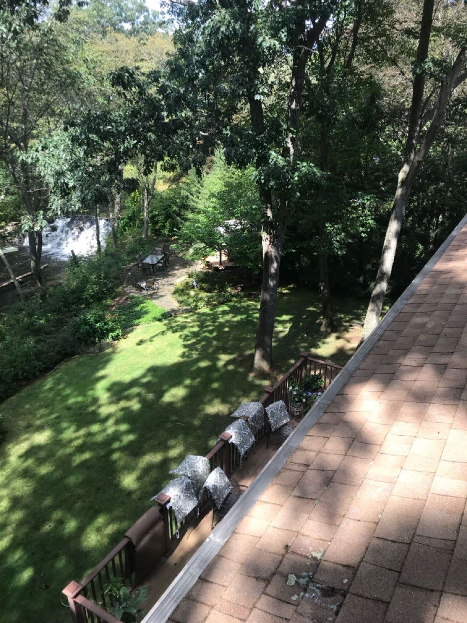 An elevated, angled view of a roof edge overlooking a wooded backyard with a deck and lawn.