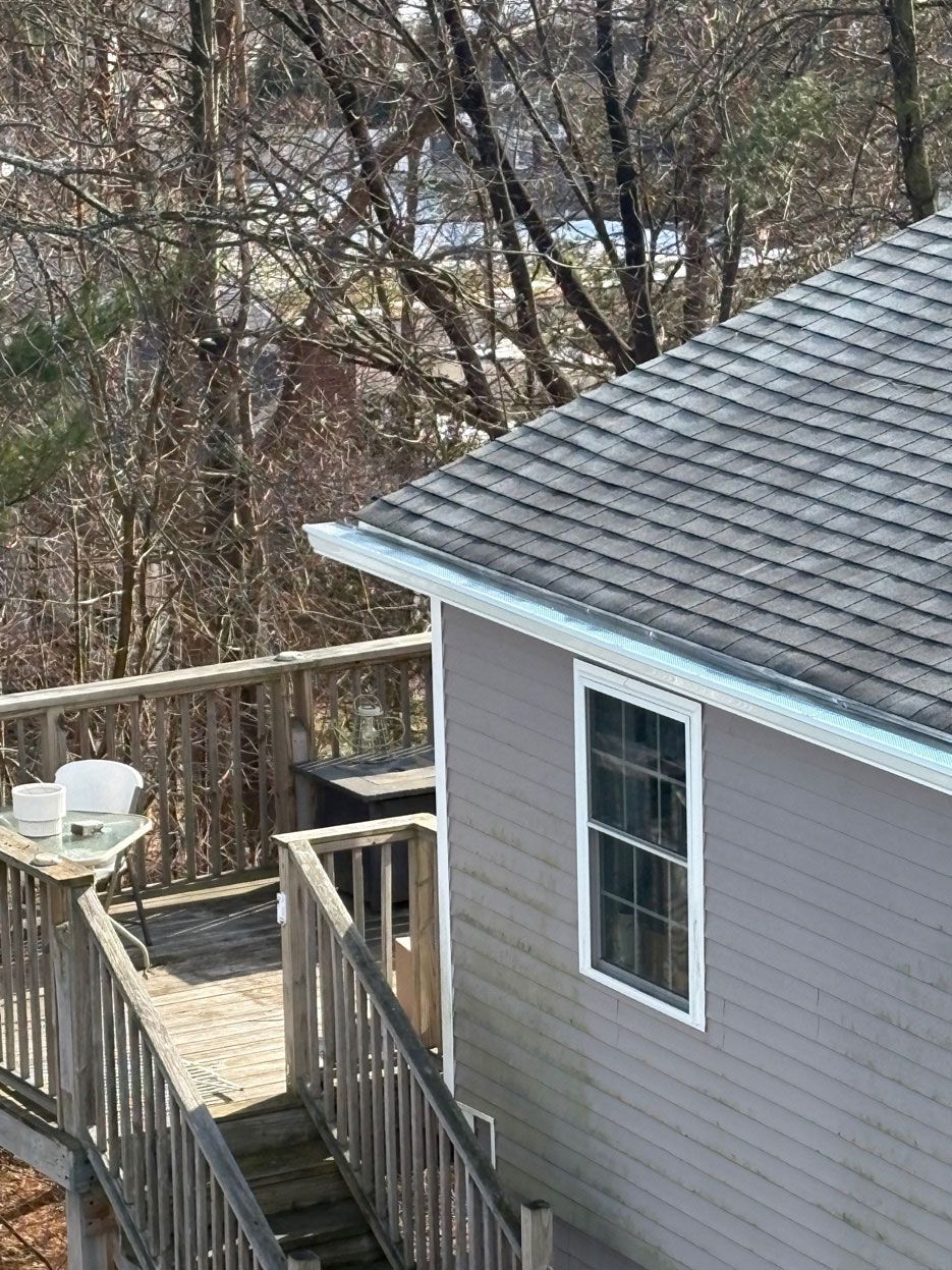 An elevated wooden deck attached to a gray house, viewed from above, with bare trees in the background.