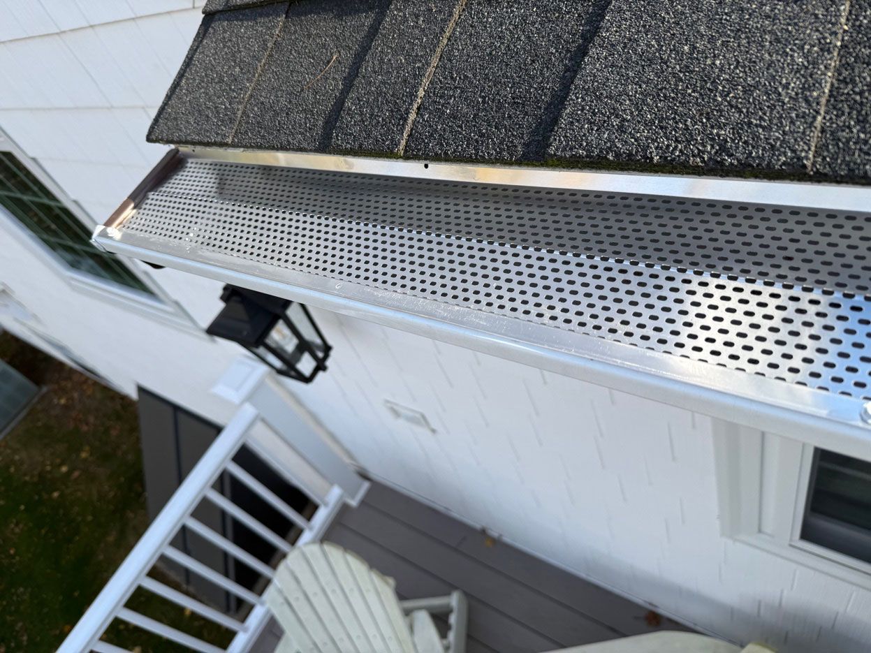 Metal gutter guard installed on a residential roof edge above a deck and white siding.