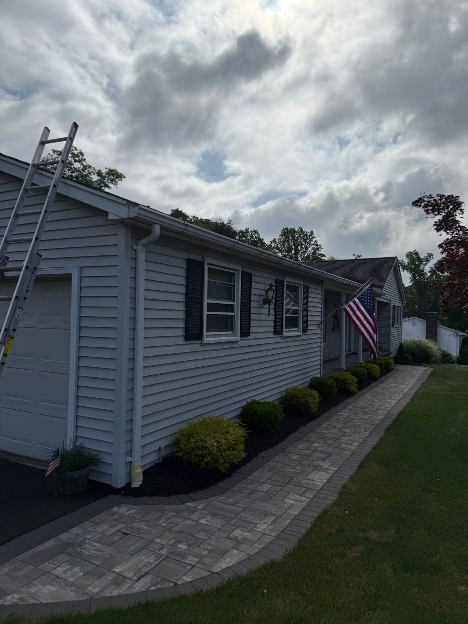A gray, single-story house with black shutters, a paver walkway, and an American flag near the front entrance.